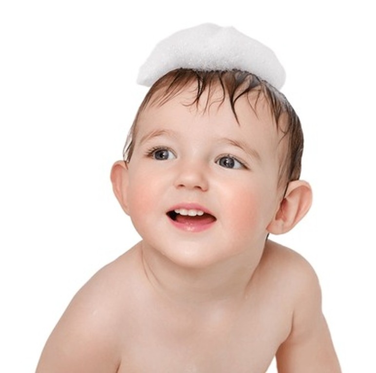 A smiling toddler with brown hair looking up, featuring a dollop of white soap suds on their head.